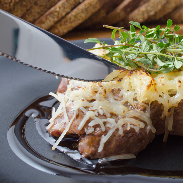 A Walco stainless steel steak knife cutting into a piece of meat with cheese and herbs.