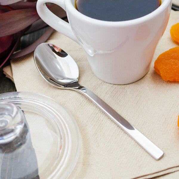 A cup of coffee with a Walco stainless steel demitasse spoon on a napkin next to it.