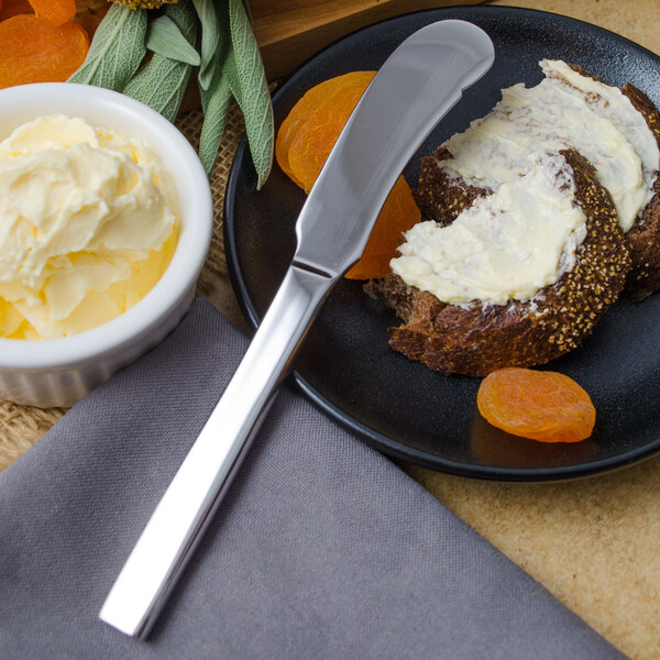 A plate with a Walco stainless steel butter knife on it with food and fruit, next to a bowl of butter.