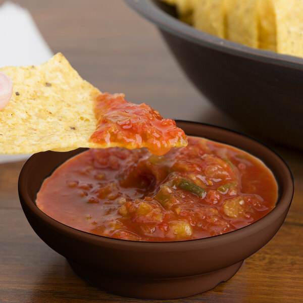 A tortilla chip in brown salsa in a brown bowl.