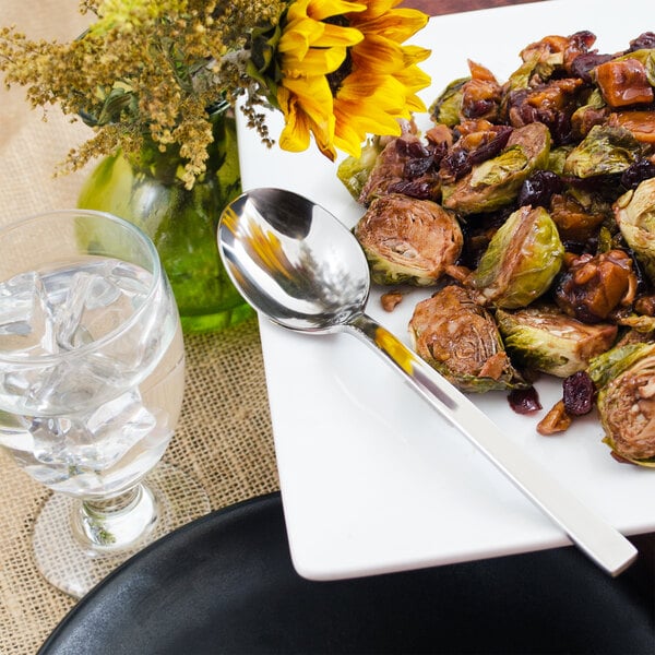 A plate of food with a Walco stainless steel serving spoon and a glass of water next to a flower.