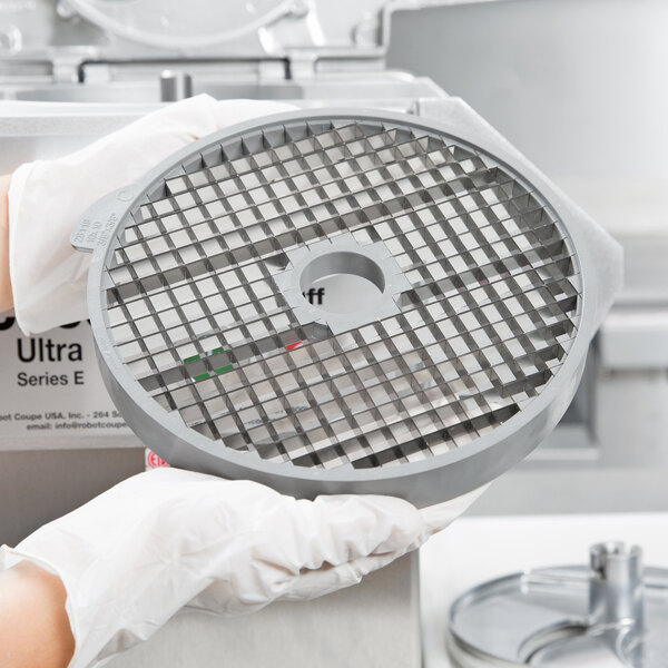 A person in white gloves holding a circular metal container with five circular discs inside.
