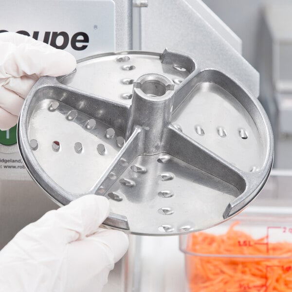 A gloved hand uses a Robot Coupe LP5DISC to cut carrots into a plastic container.