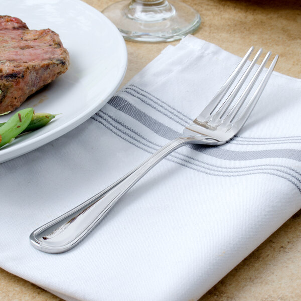 A Walco Pacific Rim stainless steel dinner fork on a plate of food.