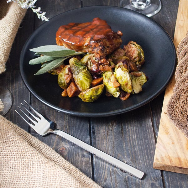 A Walco Erik stainless steel dinner fork next to a plate of food with brussels sprouts.