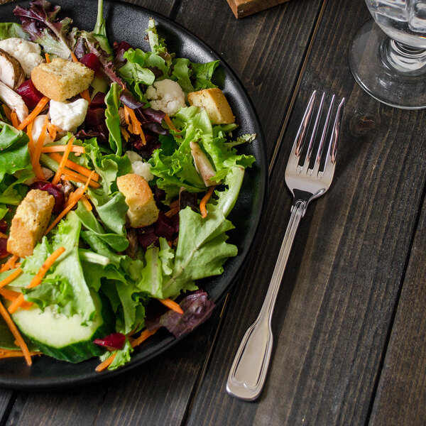 A plate of salad with a Walco Luxor stainless steel salad fork on a table.