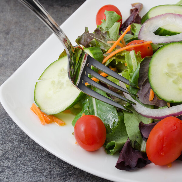 A Walco Pacific Rim stainless steel salad fork in a salad on a plate.