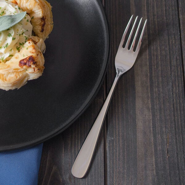 A plate with food on it next to a Walco Star stainless steel dinner fork.