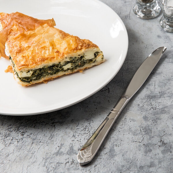 A Walco stainless steel table knife next to a piece of cheese and spinach pie on a plate.