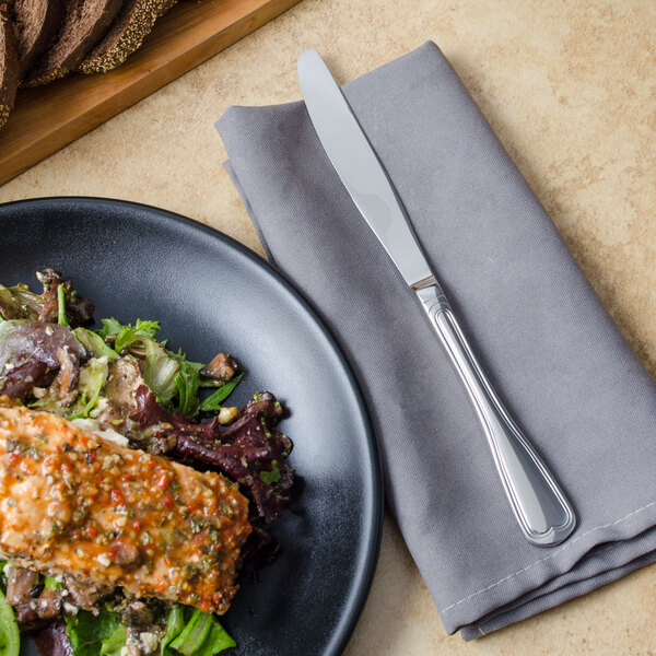 A plate of food next to a Walco Luxor table knife and napkin.