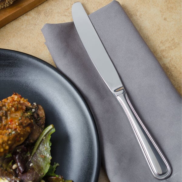 A Walco Pacific Rim table knife on a napkin next to a plate of food.