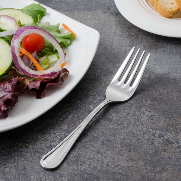 A Walco Pacific Rim stainless steel salad fork on a plate of salad.