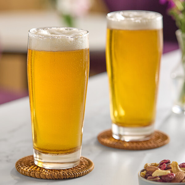 Two Arcoroc Willi Becher pub glasses of beer on a table with nuts.