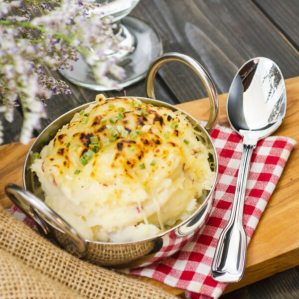 A Walco Luxor stainless steel teaspoon in a bowl of mashed potatoes on a wooden board.