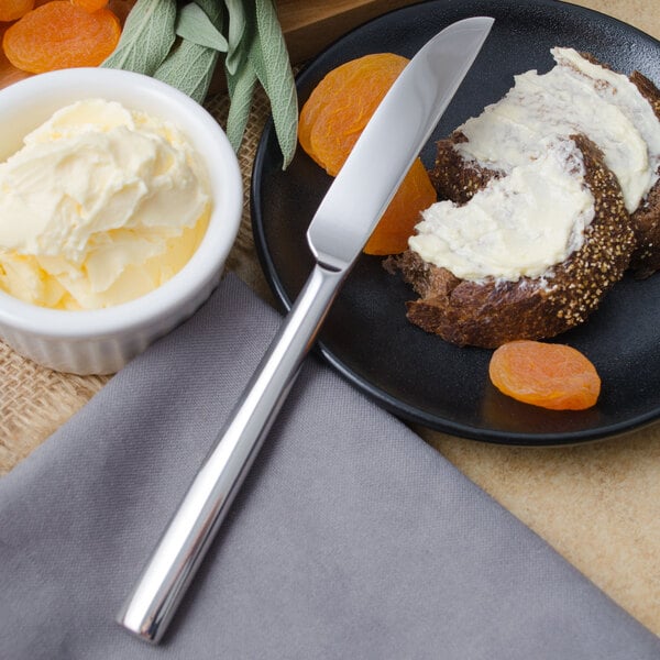 A Walco stainless steel butter knife on a plate with bread and fruit.