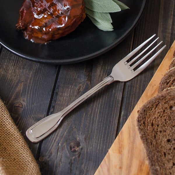 A Walco Luxor stainless steel table fork next to a plate of food with a piece of meat and bread.