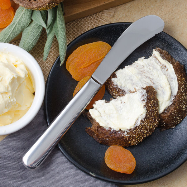 A plate of food with a Walco stainless steel butter spreader and a bowl of butter.