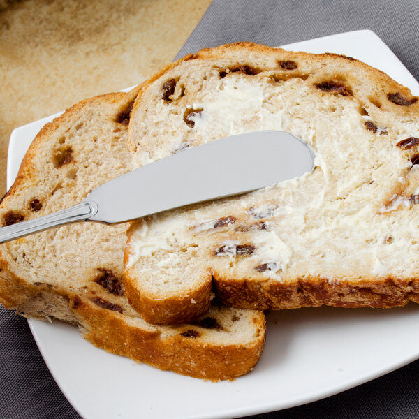 A Walco stainless steel butter spreader on a piece of bread with butter.