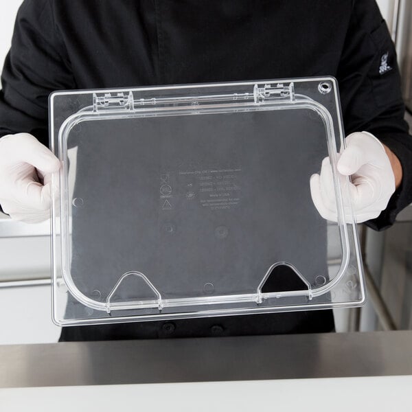 A person in a chef's uniform holding a Carlisle clear plastic container with a hinged lid.