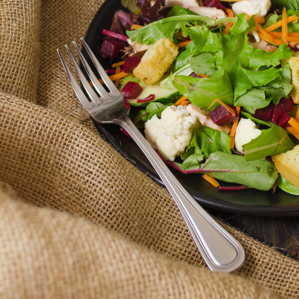 A Walco Lisbon stainless steel salad fork next to a plate of salad.