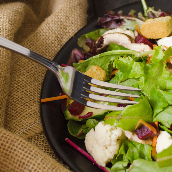A Walco stainless steel salad fork on a plate of salad with chicken and vegetables.