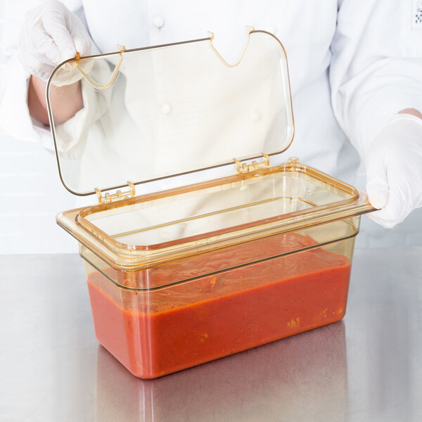 A person holding a Carlisle amber high heat hinged lid over a container of food.