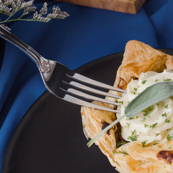 A Walco Danish Pride stainless steel dinner fork spearing a pastry on a white plate.
