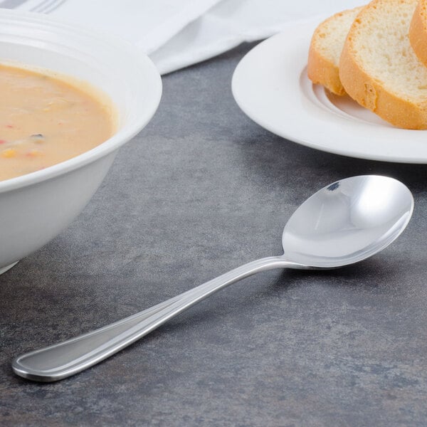 A bowl of soup with a Walco heavy weight bouillon spoon next to a plate of bread on a table.