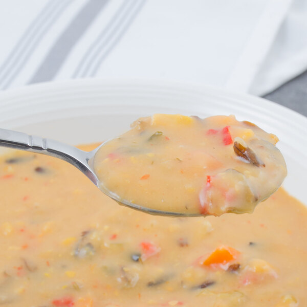 A Walco Meteor stainless steel large bowl bouillon spoon filled with soup over a white background.