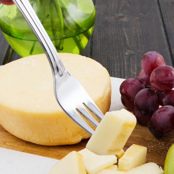 A Walco stainless steel cocktail fork spearing a piece of cheese on a plate.