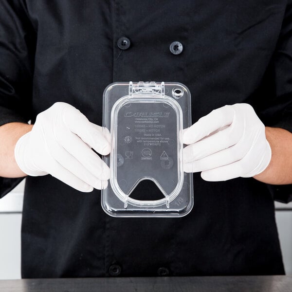 A person wearing gloves holding a Carlisle clear plastic container with a hinged lid.