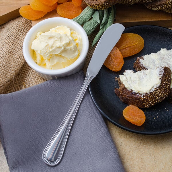 A plate with a butter spreader on it and a bowl of butter.