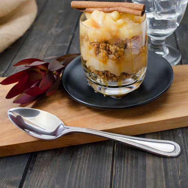 A glass of dessert with granola and caramel sauce with a Walco stainless steel dessert spoon.