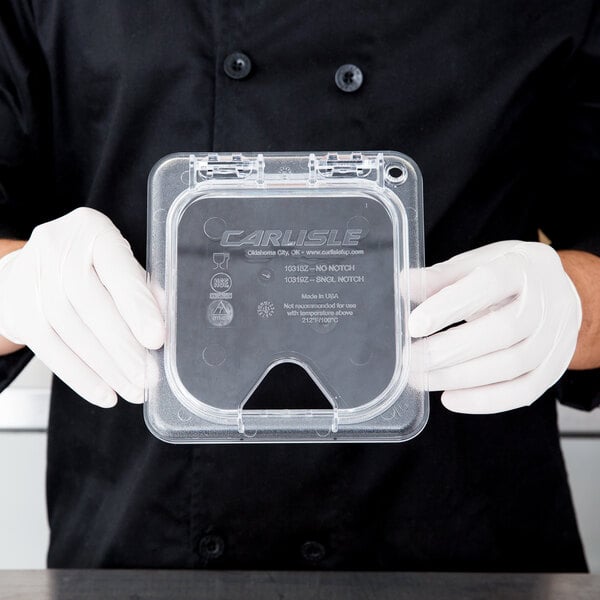 A person in white gloves holding a Carlisle clear plastic container with a hinged lid.