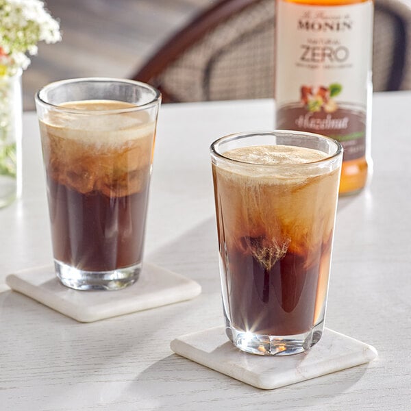 Two glasses of Monin hazelnut flavored brown liquid on coasters.