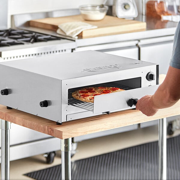 A person putting a pizza into an Avantco countertop pizza oven.