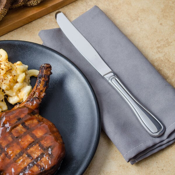 A plate of grilled meat with a Walco Saville dinner knife and macaroni and cheese.