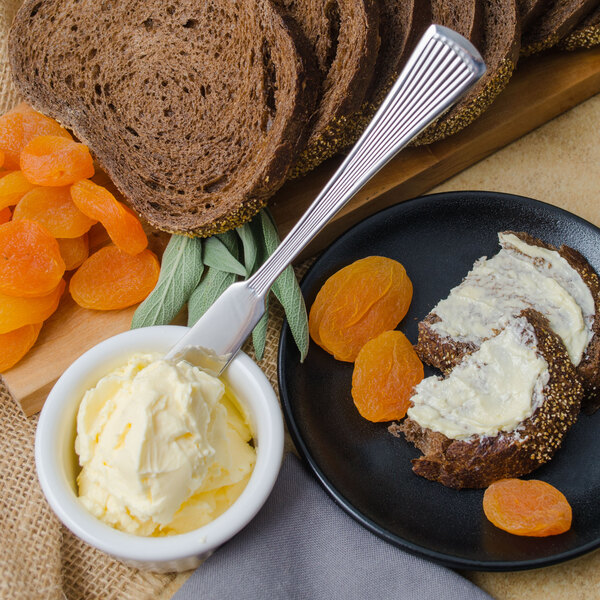 A Walco Bosa Nova stainless steel butter spreader with a plate of bread and butter.