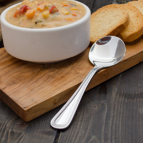 A bowl of soup with a Walco stainless steel bouillon spoon on a cutting board.