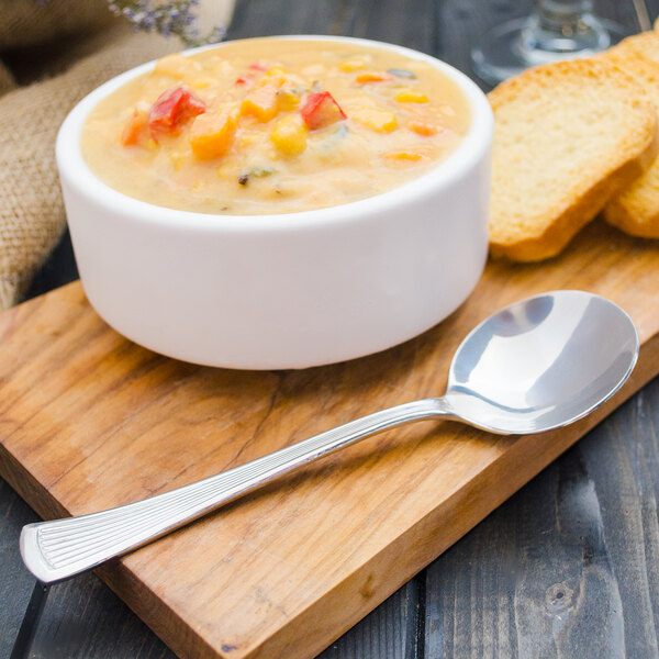 A Walco stainless steel bouillon spoon in a bowl of soup on a wooden surface.