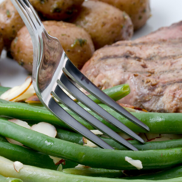A Walco stainless steel dinner fork holding meat and green beans on a plate.