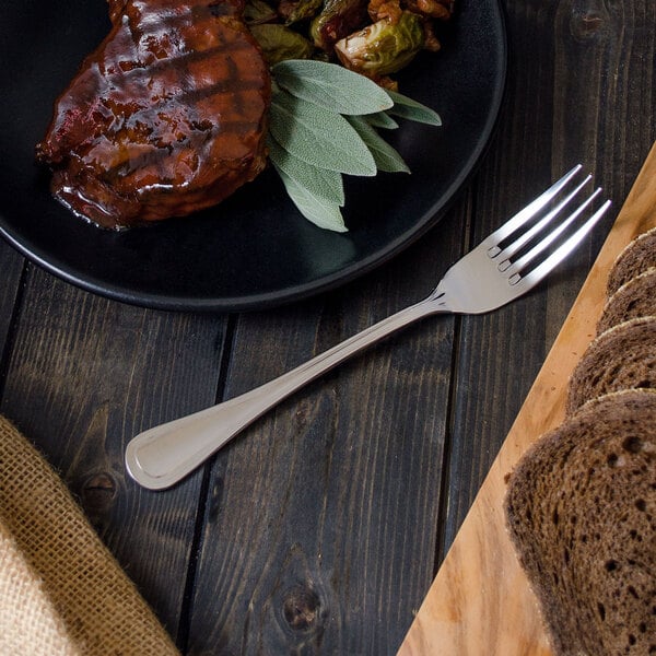 A Walco Lisbon table fork on a plate of meat and bread.