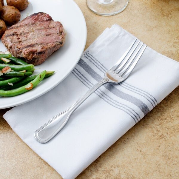 A Walco Saville European fork on a plate with steak, potatoes, and a napkin.