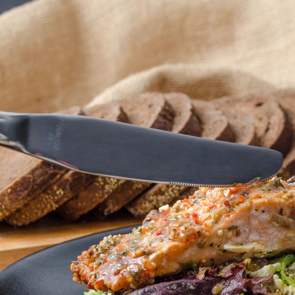A Walco Balance stainless steel table knife cutting salmon on a plate.