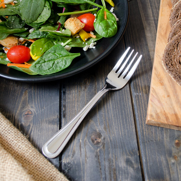 A Walco stainless steel salad fork on a plate of salad.
