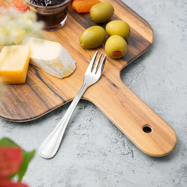 A Walco Marcie stainless steel cocktail fork on a wooden board with cheese and olives.