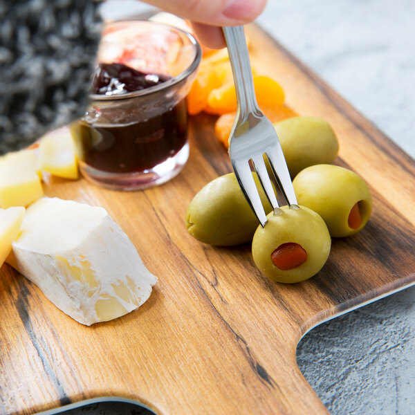 A person holding a Walco Marcie stainless steel cocktail fork over a plate of cheese, olives, and jam.