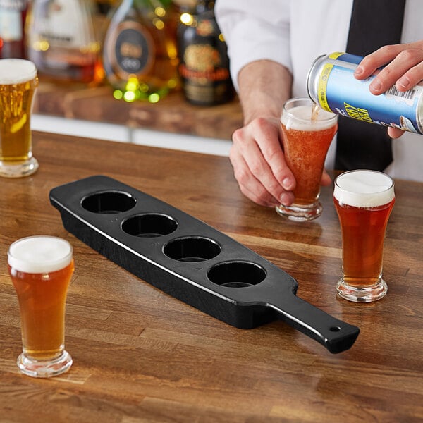 A black Libbey melamine tasting flight paddle with six beer glasses on it and a hand holding a glass of beer.