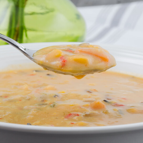 A Walco Barony stainless steel bouillon spoon holding soup over a bowl.