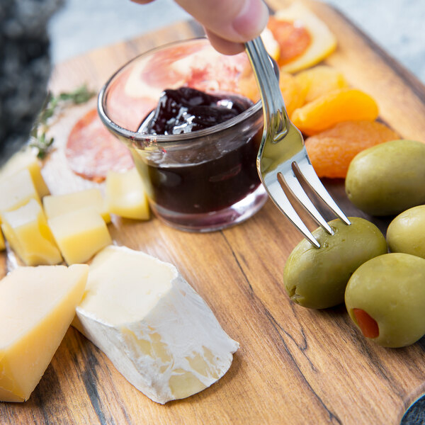 A person holding a Walco Barony stainless steel cocktail fork over a plate of food.
